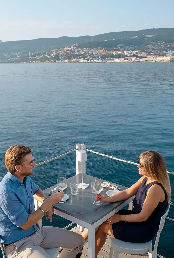Casal jantando à mesa no convés de um iate, com o mar ao fundo